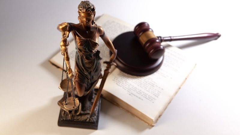 Vrouwe Justitia met weegschaal naast een rechtershamer op een opengeslagen boek