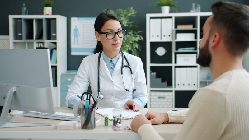 Arts in witte jas in gesprek met een patient in de spreekkamer