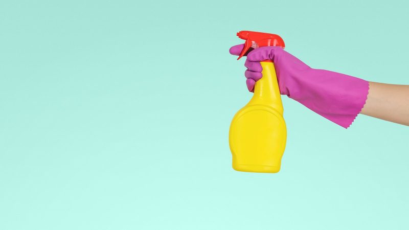 Hand met schoonmaakhandschoen houdt een sprayfles vast