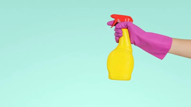 Hand met schoonmaakhandschoen houdt een sprayfles vast