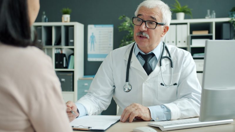 Zorgverlener in witte jas in gesprek met een patiënt in de spreekkamer