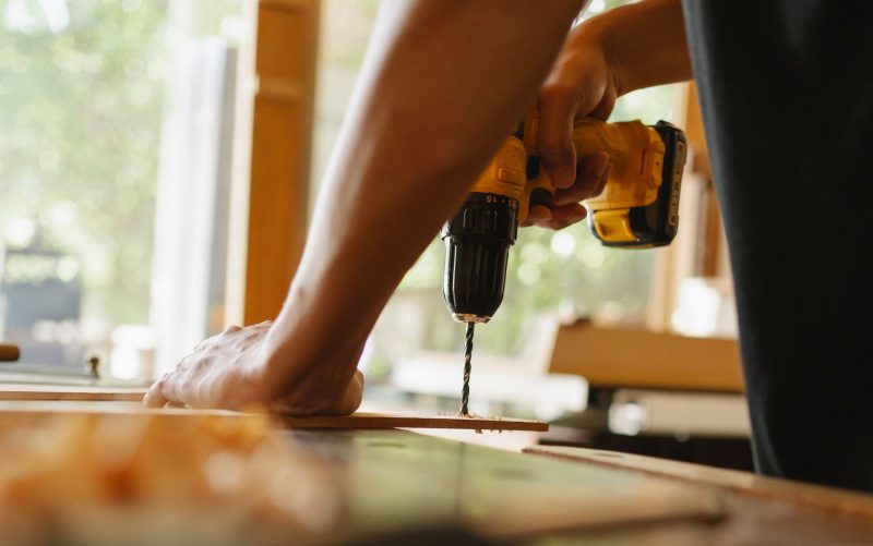 Klusjesman boort in een houten plank, beeld bij online marketing voor klusbedrijven