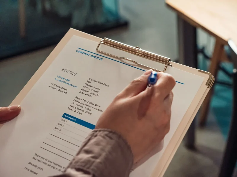 Website laten maken incassobureau: factuur op een klembord wordt ingevuld